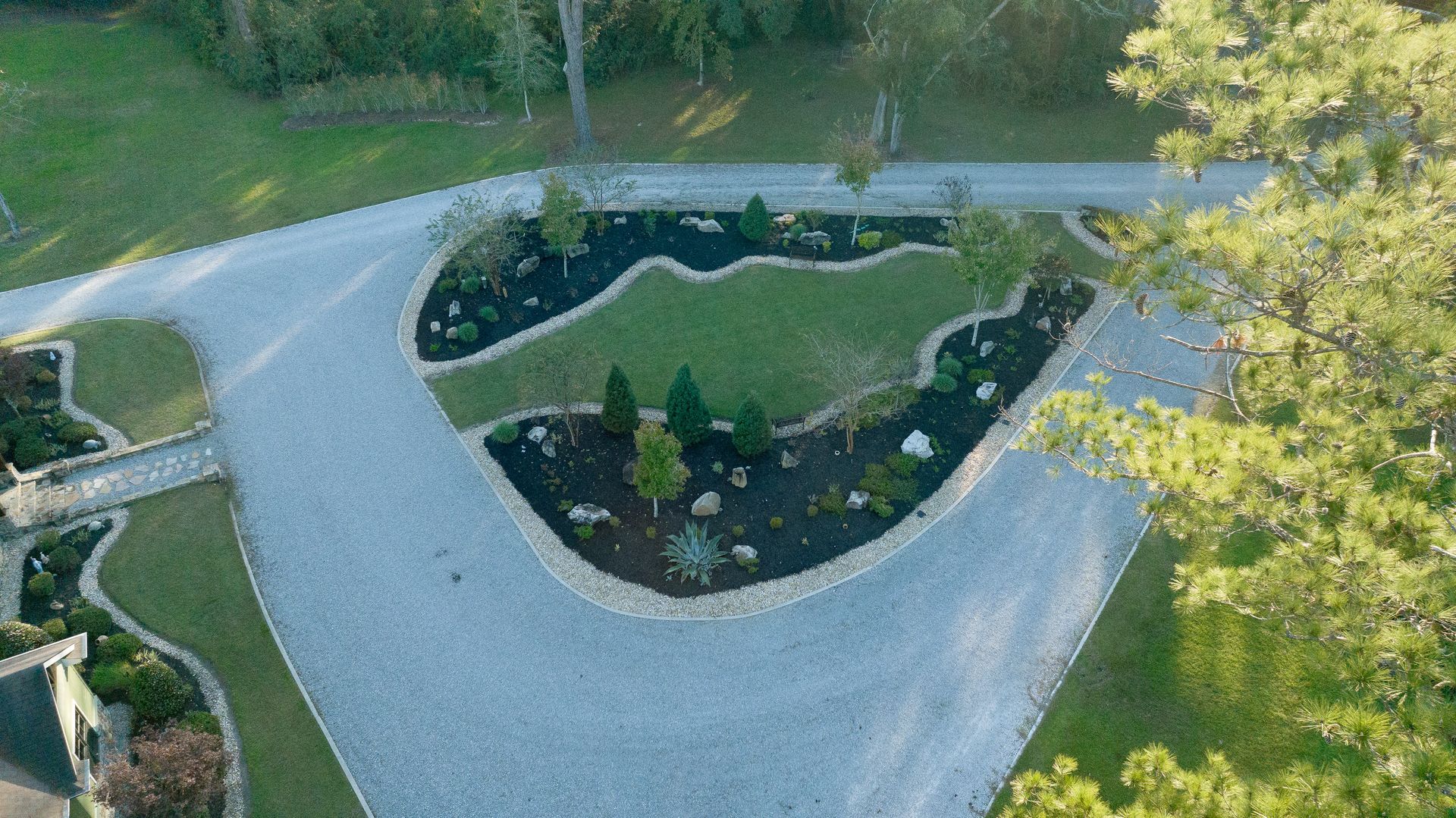 Aerial view of a curved gravel driveway around a landscaped island with shrubs and trees
