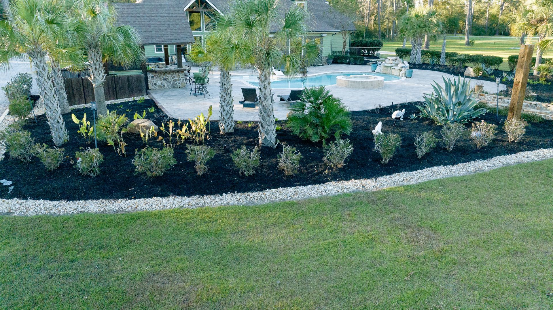 Backyard patio with a pool, lounge chairs, and landscaped shrubs bordering a green lawn