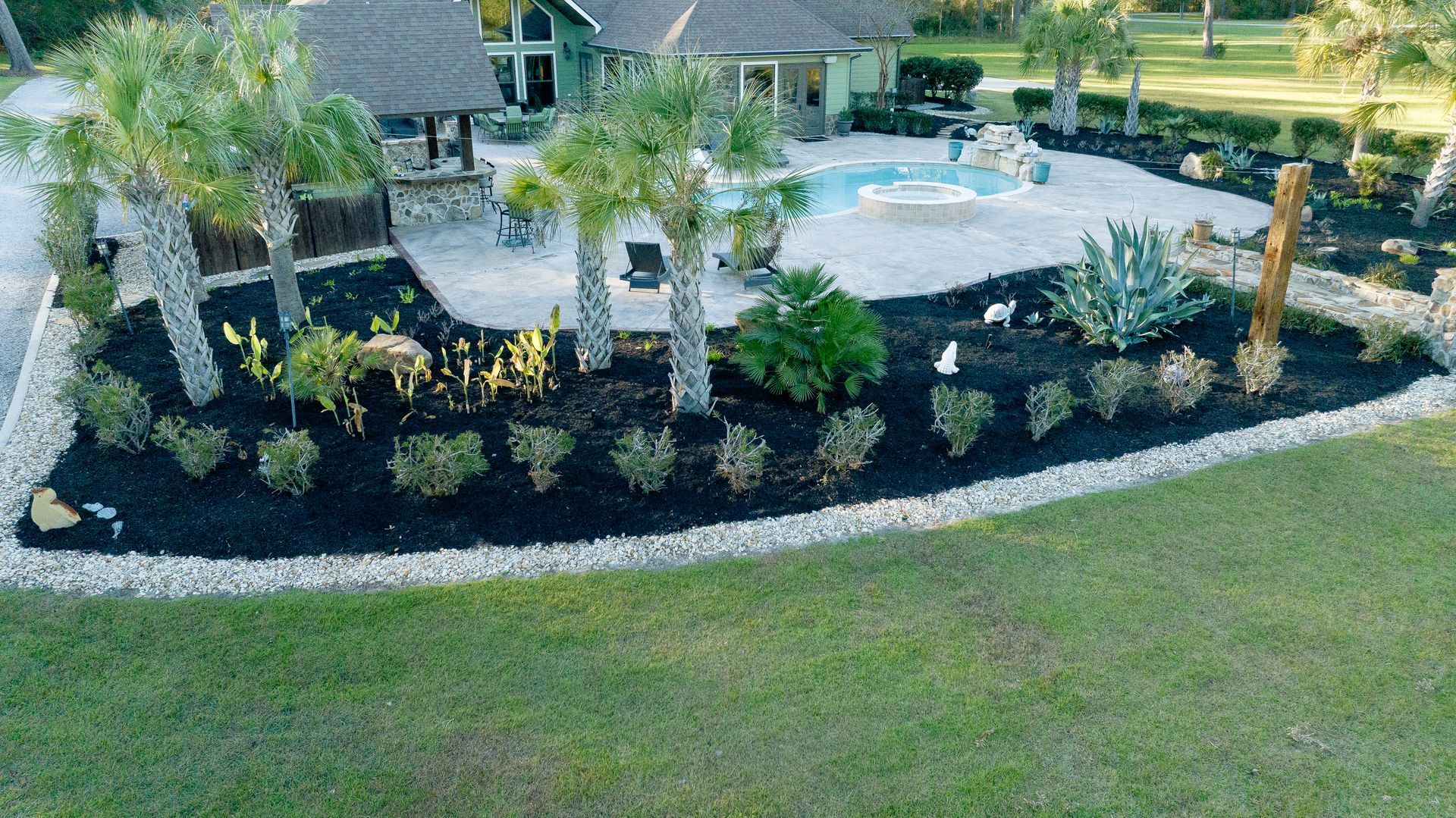 Aerial view of a landscaped backyard with a stone patio, palm trees, and neatly trimmed shrubs.