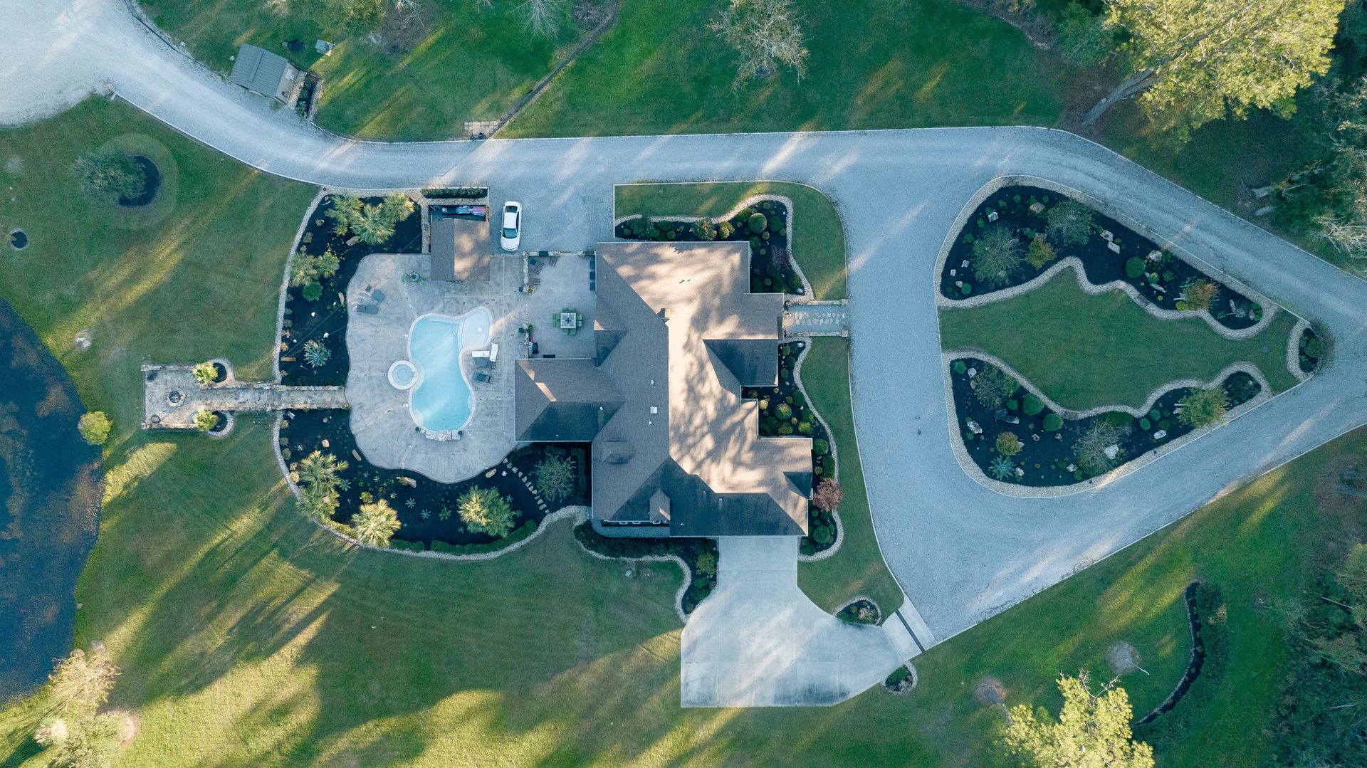 Aerial view of a house with a driveway, surrounded by green grass and trees.