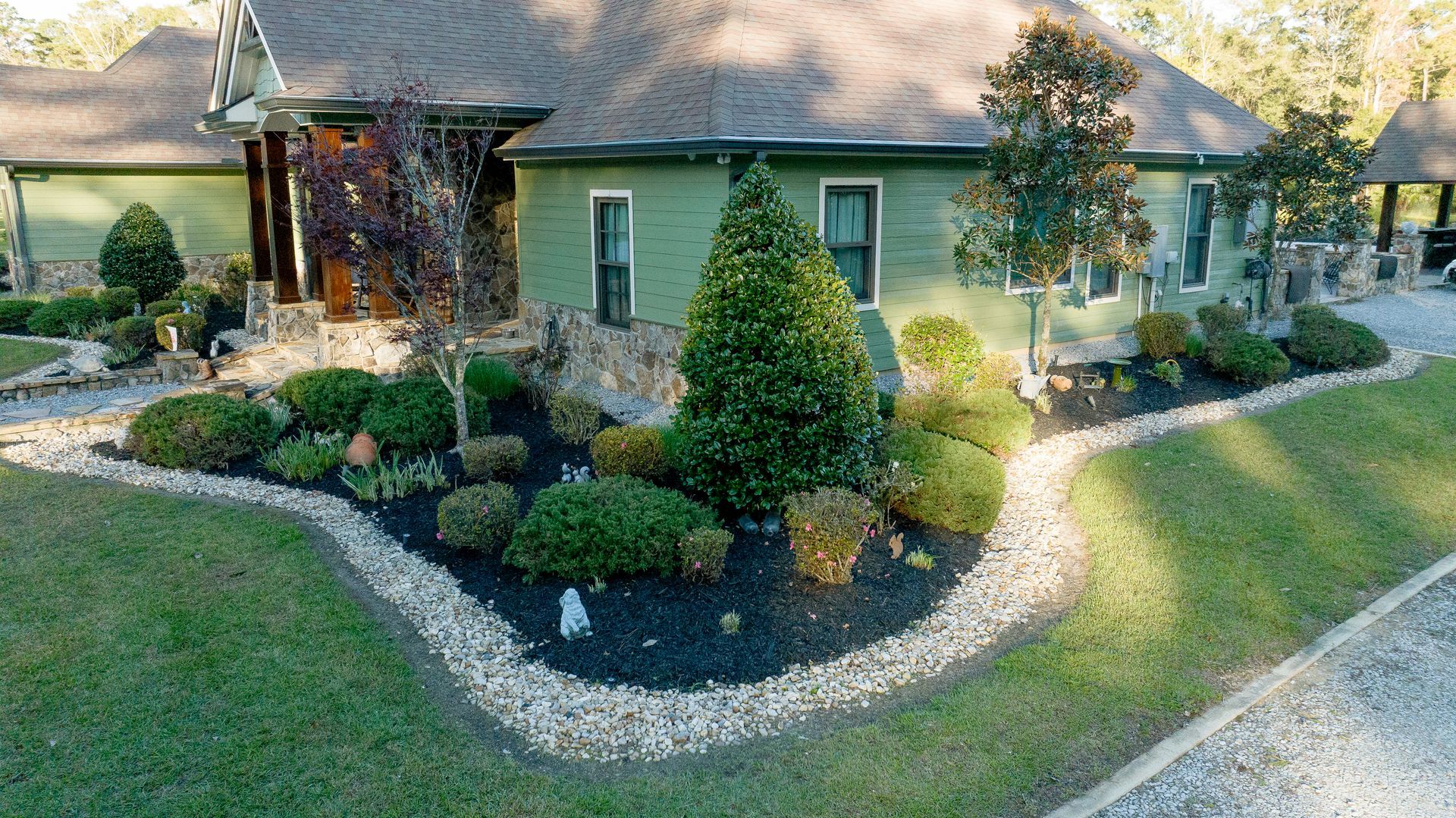 Landscaped front yard with shrubs, flowers, and a green house with a stone entryway