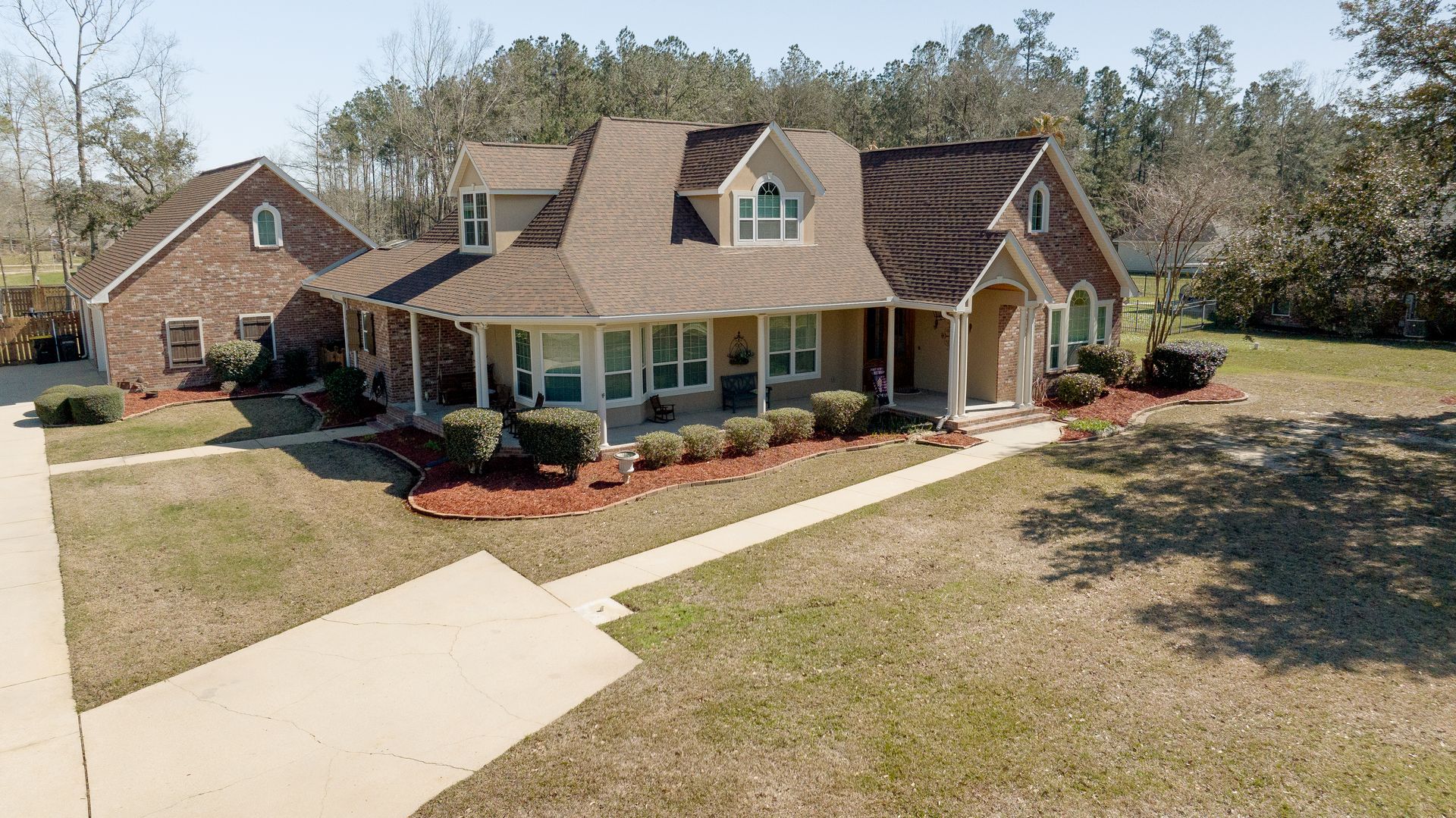 Suburban brick house with a covered porch, driveway, and landscaped front yard on a sunny day