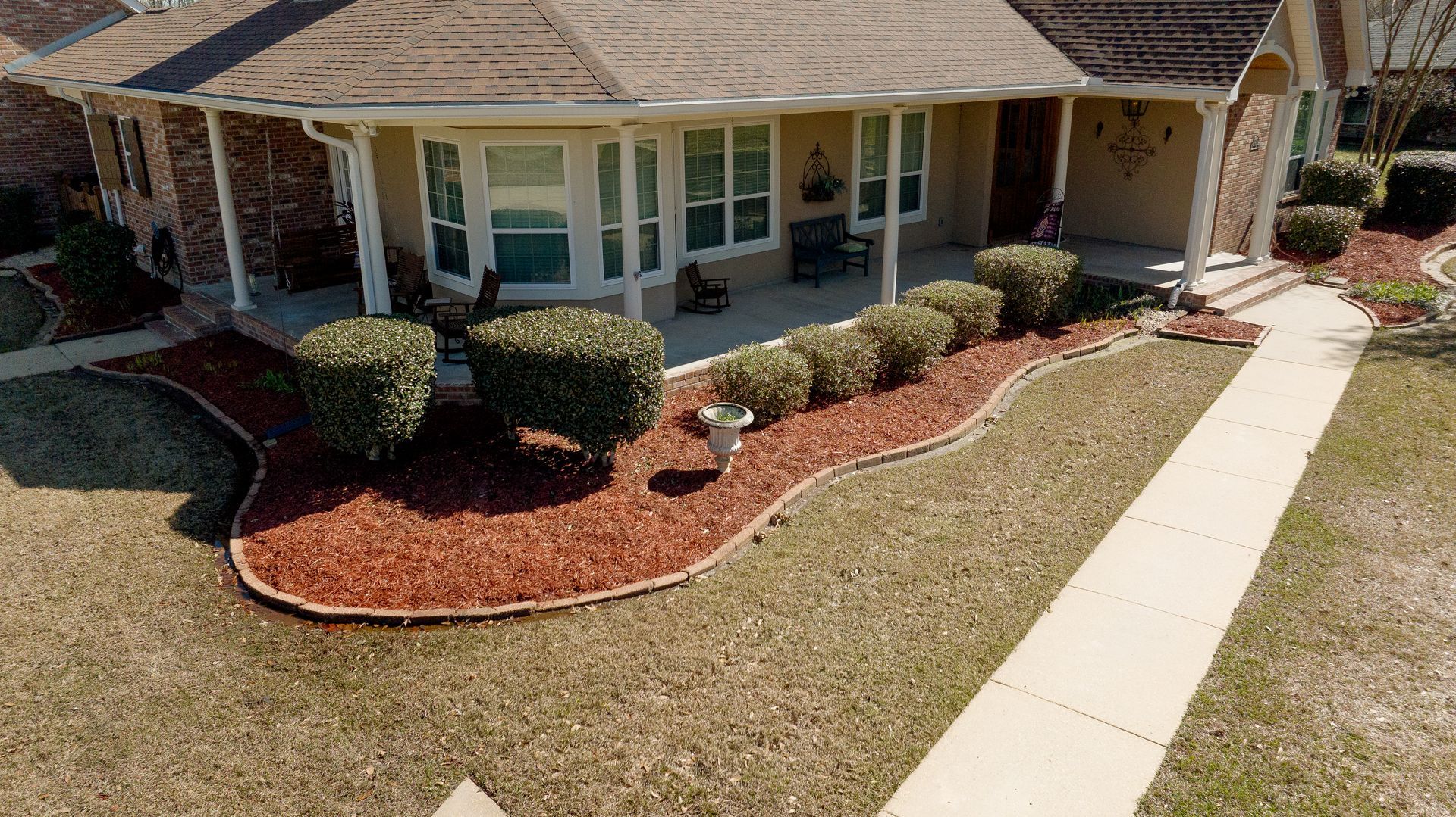 Suburban house with a front porch, trimmed shrubs, and a curved sidewalk leading to the entrance
