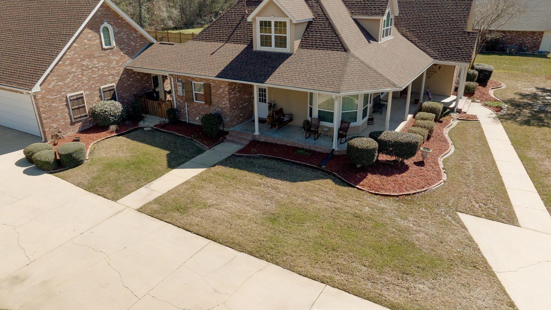 Suburban house with a covered front porch, driveway, and neatly landscaped yard from an aerial view