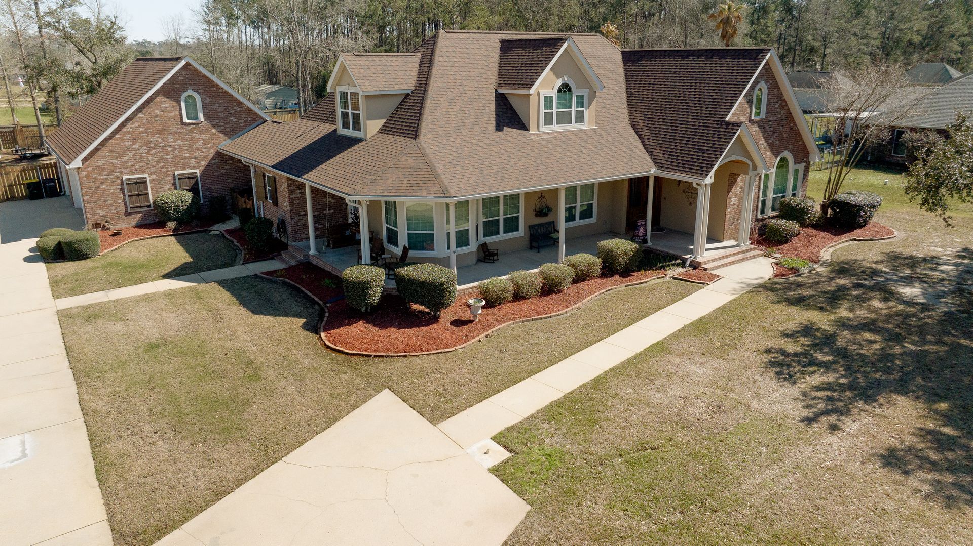 Aerial view of a brick suburban house with a front porch, landscaped yard, and driveway.