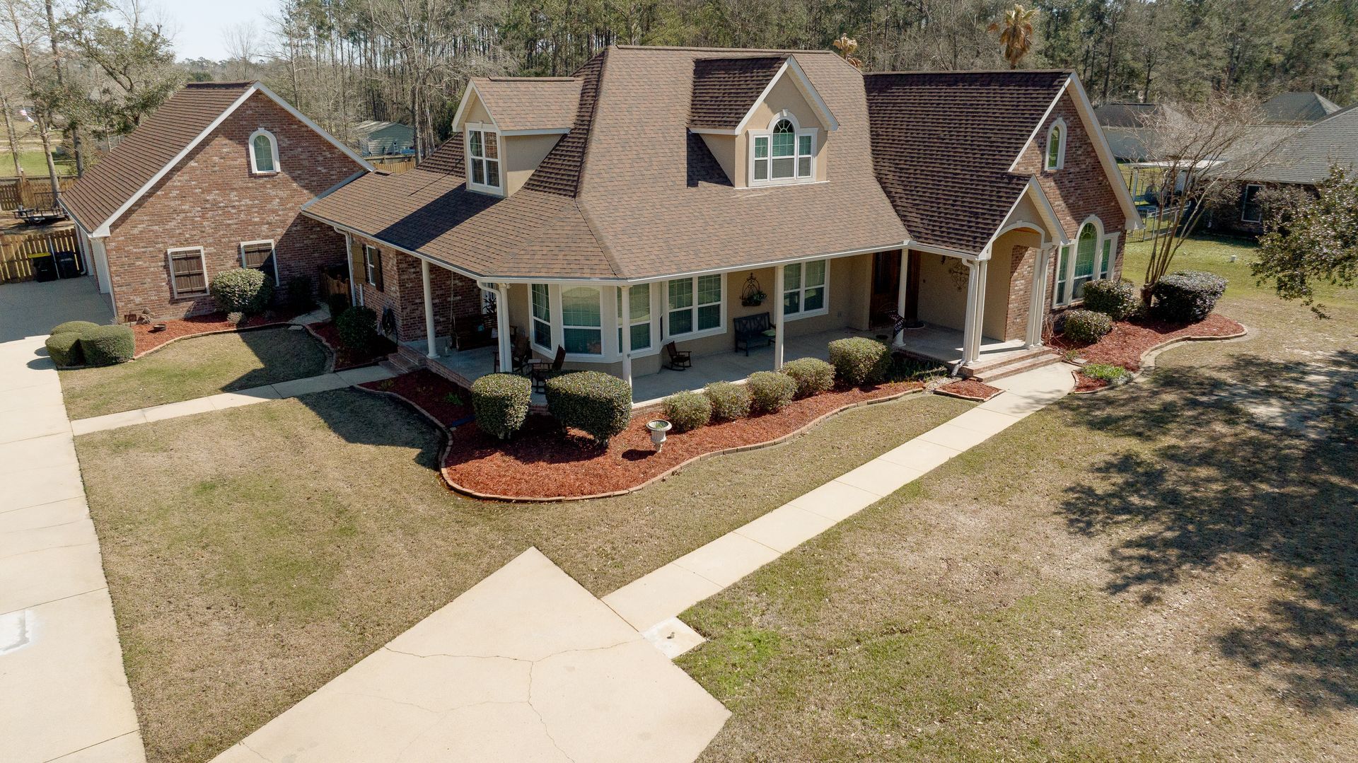 Suburban brick house with brown roof, white-trim windows, and landscaped front yard from above