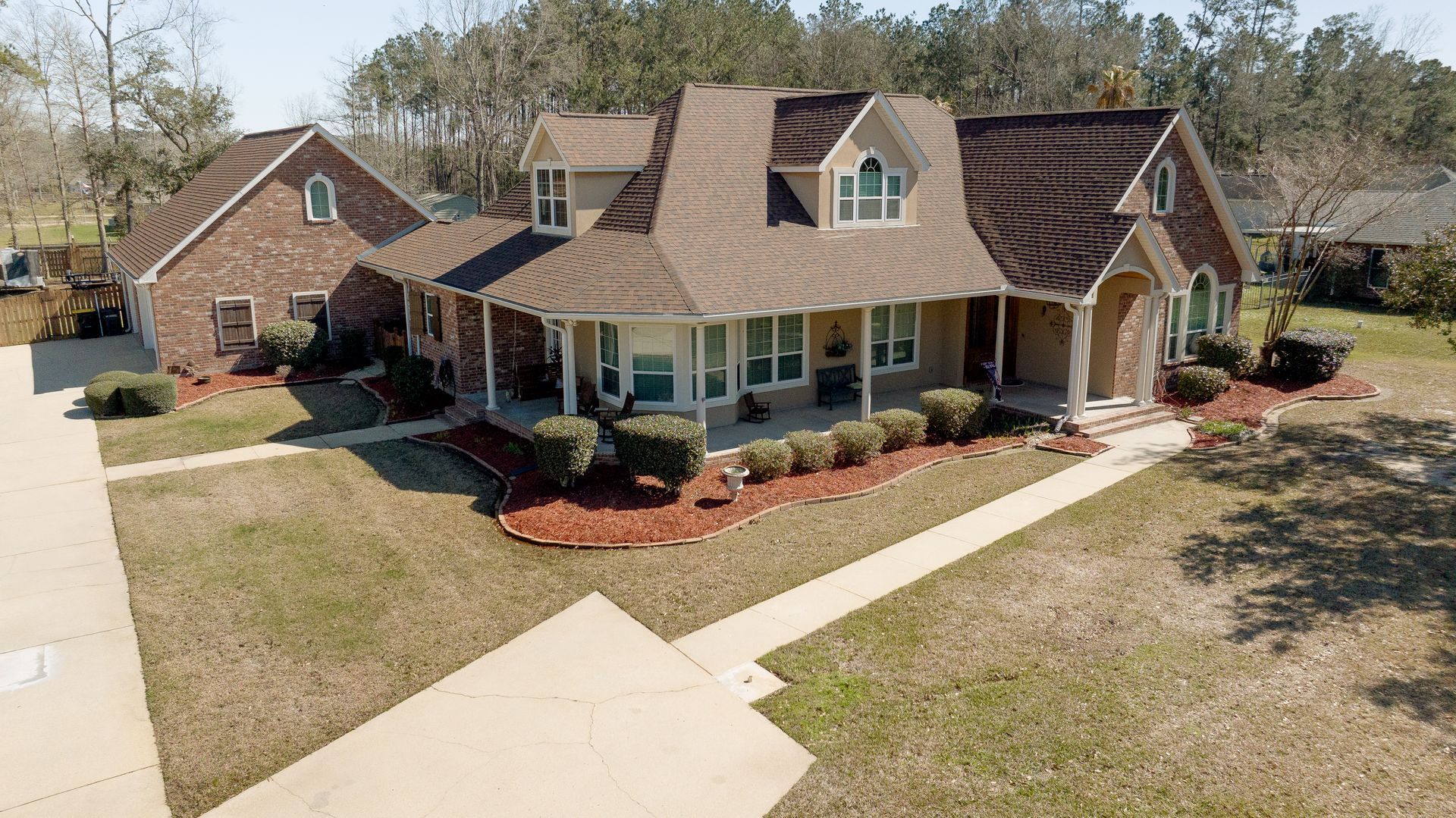 Brick suburban house with brown roof, front porch, and landscaped yard on a sunny day