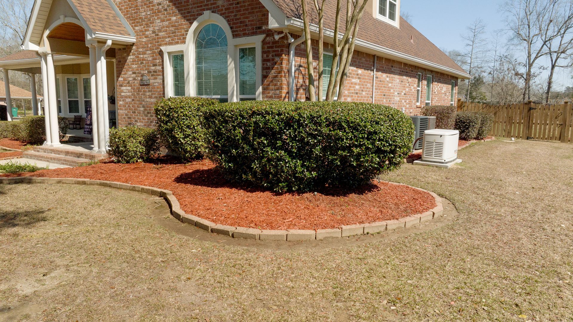 Brick house front yard with arched windows, trimmed shrubs, and red mulch landscaping