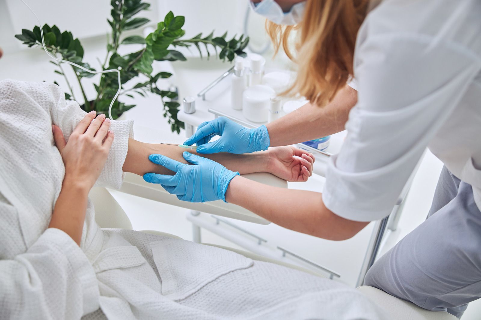 Person receiving an intravenous injection in arm by person wearing gloves in a clinic setting.