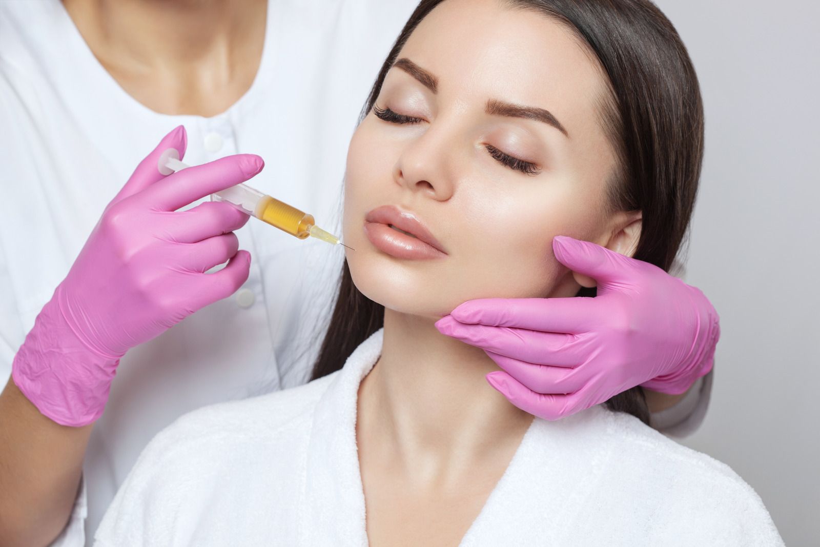 Person receiving facial injection, performed by gloved hands, in a well-lit setting.