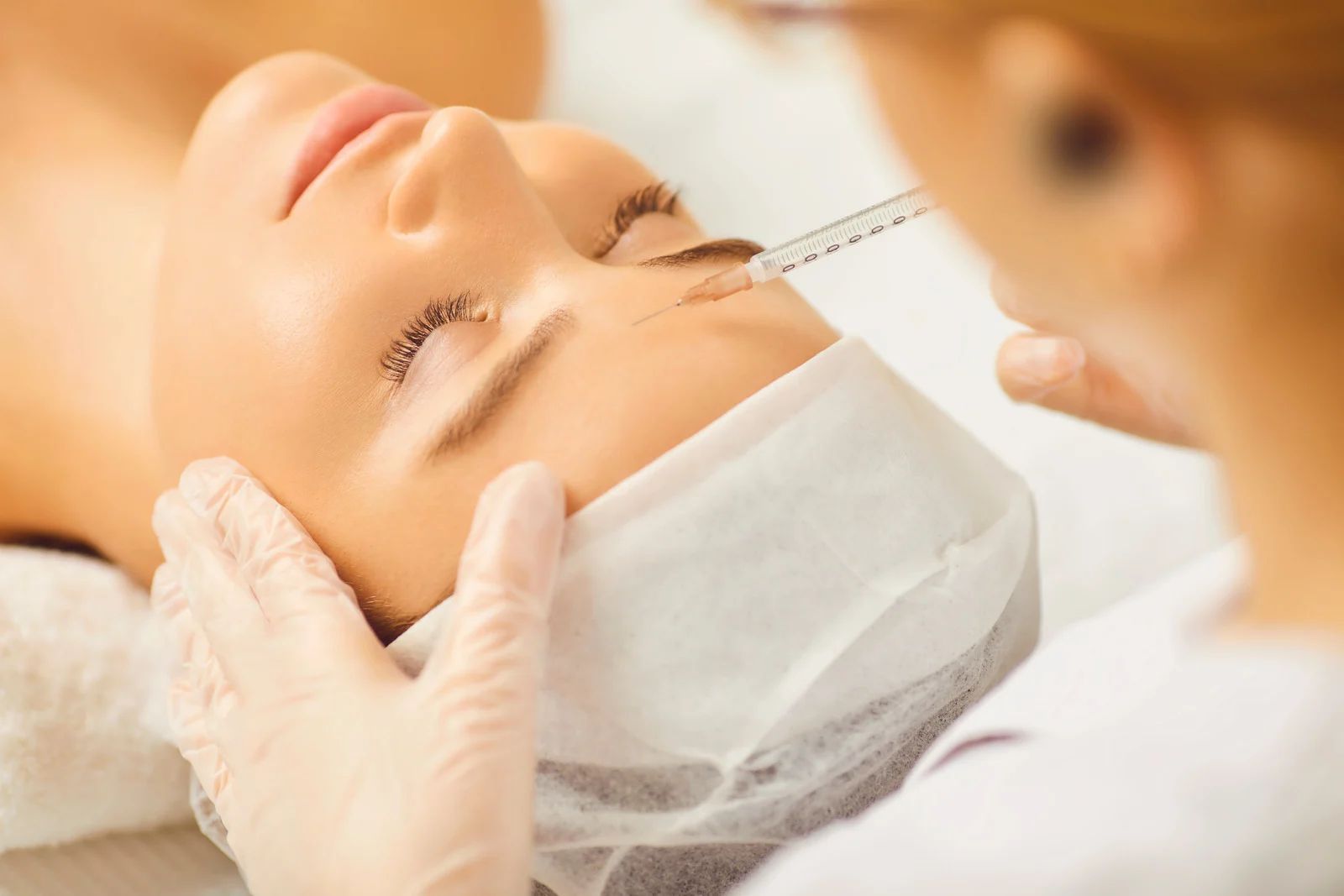 Person receiving a cosmetic injection in the forehead; white gloves, medical setting.
