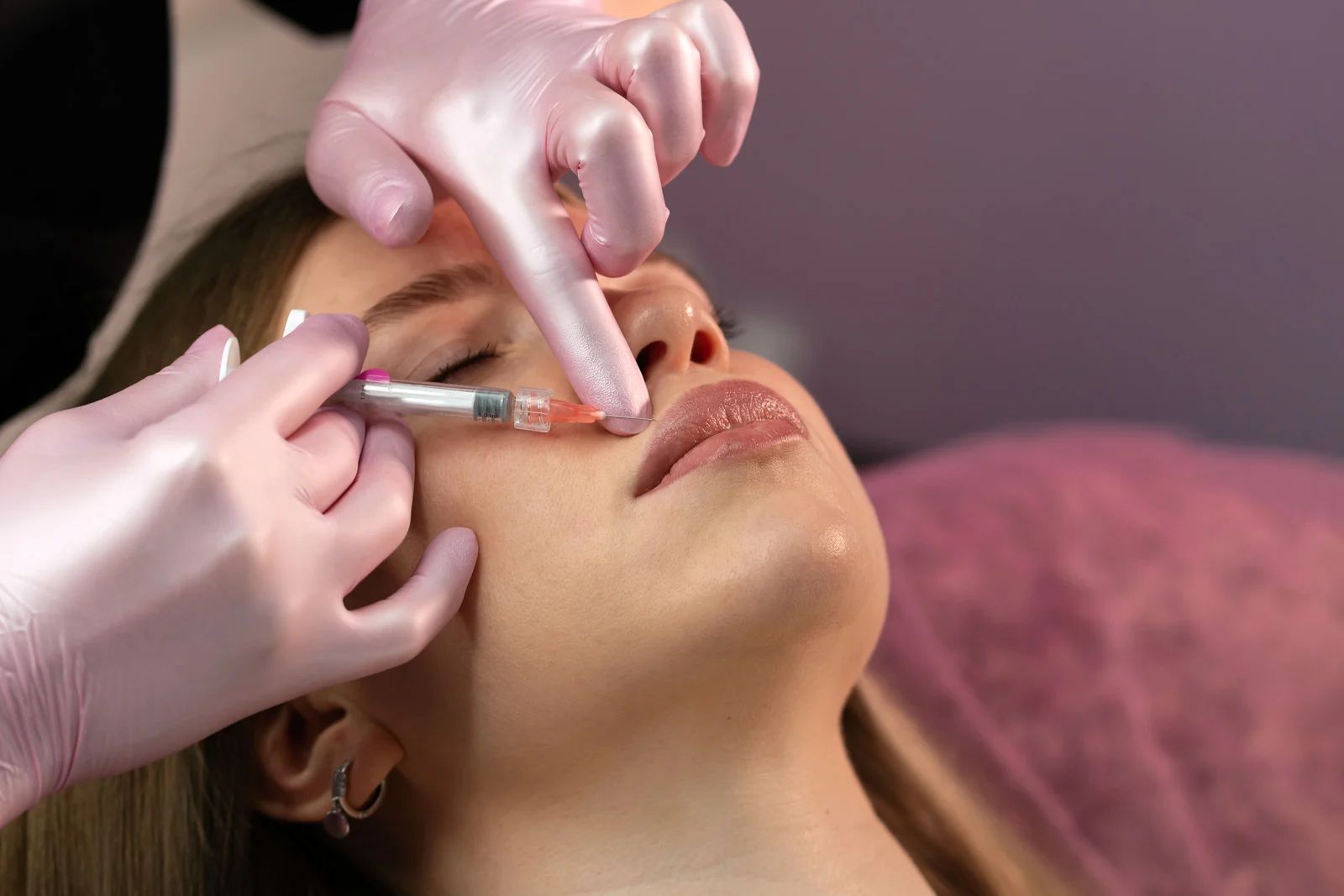 Gloved hands injecting filler into a woman’s nose and lips during a cosmetic procedure