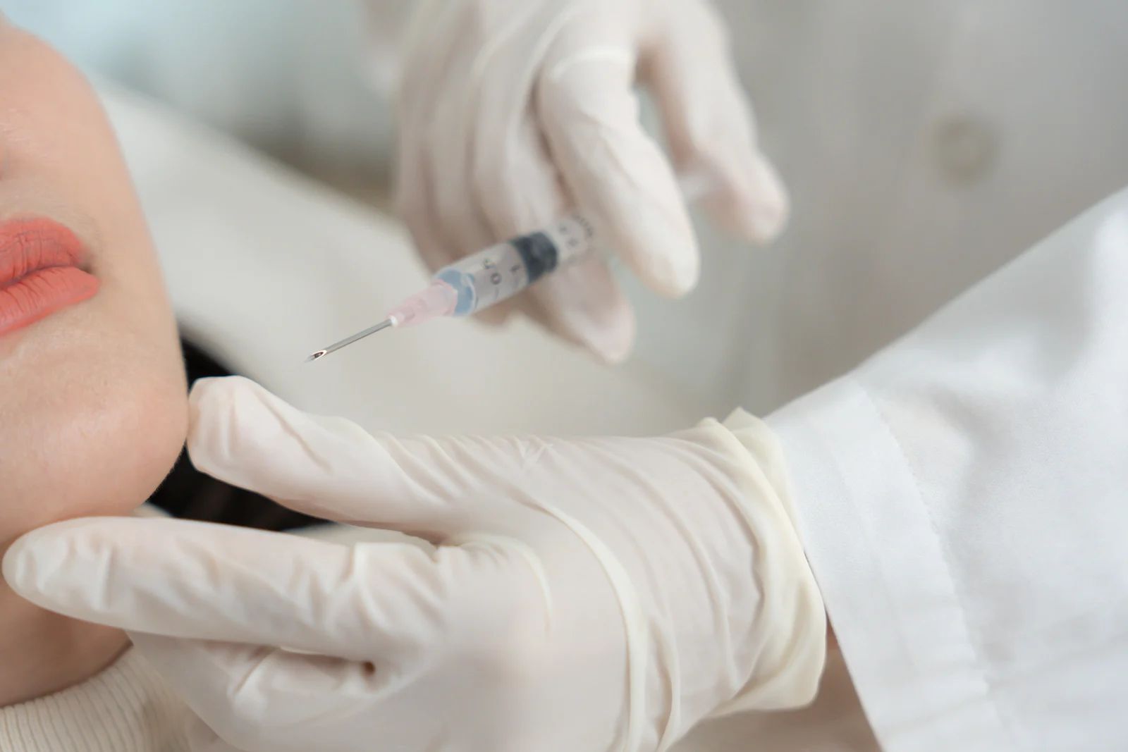Person receiving cosmetic injection in face. Gloved hand with syringe.