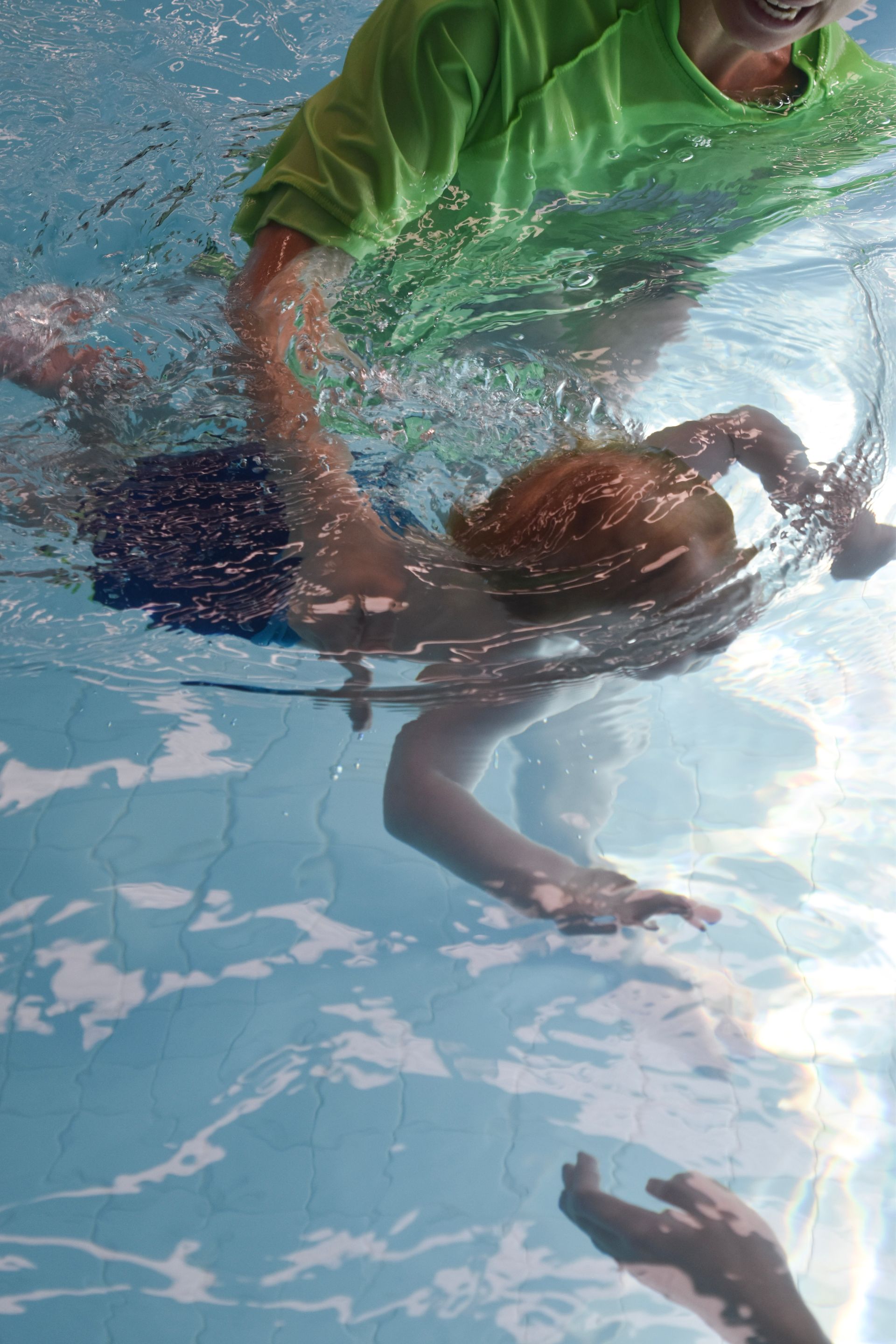 A person in a green shirt is swimming underwater in a pool.