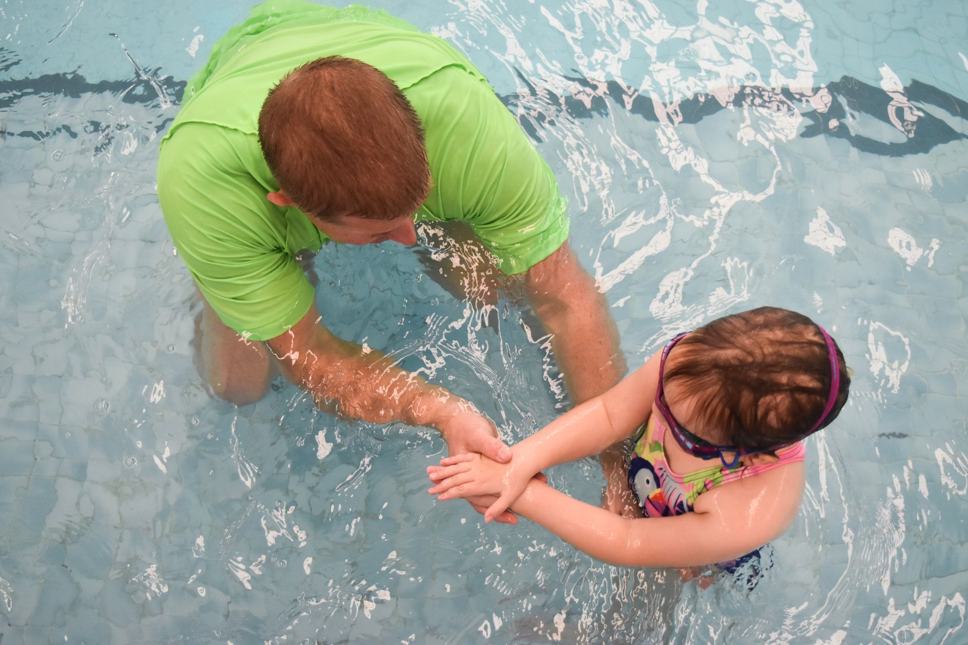 A man is helping a little girl in a swimming pool.