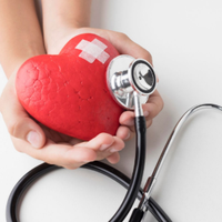 Hands holding a red heart with a bandage on it, positioned next to a medical stethoscope.