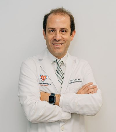 Doctor in a white coat with arms crossed, standing against a light gray background.