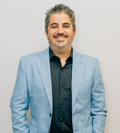 Smiling man in a light blue blazer and dark shirt against a plain light background