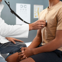 A clinician using a stethoscope to examine a patient’s chest during a medical consultation in a doctor's office.