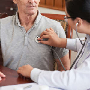 A healthcare provider in a lab coat uses a stethoscope to examine a person's chest.