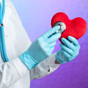 A healthcare professional in a white coat and blue gloves uses a stethoscope to examine a plush red heart.