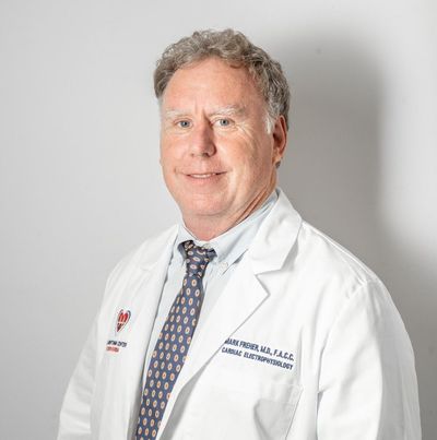 Doctor in a white coat and tie, posing against a light gray background.