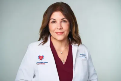 Doctor in a white coat and tie, posing against a light gray background.