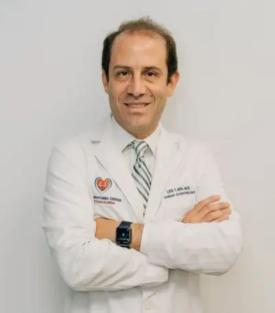 Doctor in a white coat with arms crossed, standing against a light gray background.