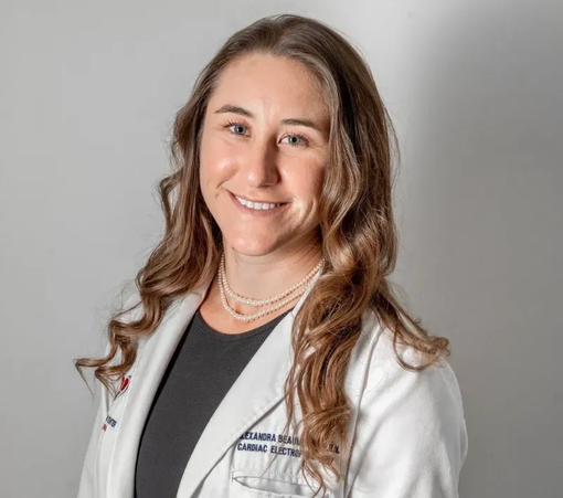 Alexandra Bell - Woman in a white lab coat smiling against a light gray background.