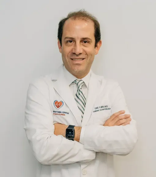 Dr. Luis Mora - Doctor in white coat with arms crossed, smiling against a plain gray background.