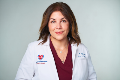 Doctor in a white coat with arms crossed, standing against a light gray background.
