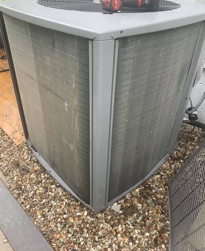 A large air conditioner is sitting on top of a pile of gravel.