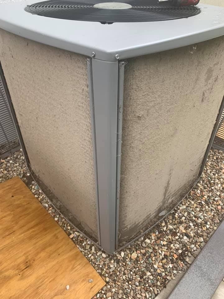 A dirty air conditioner is sitting on top of a pile of gravel.