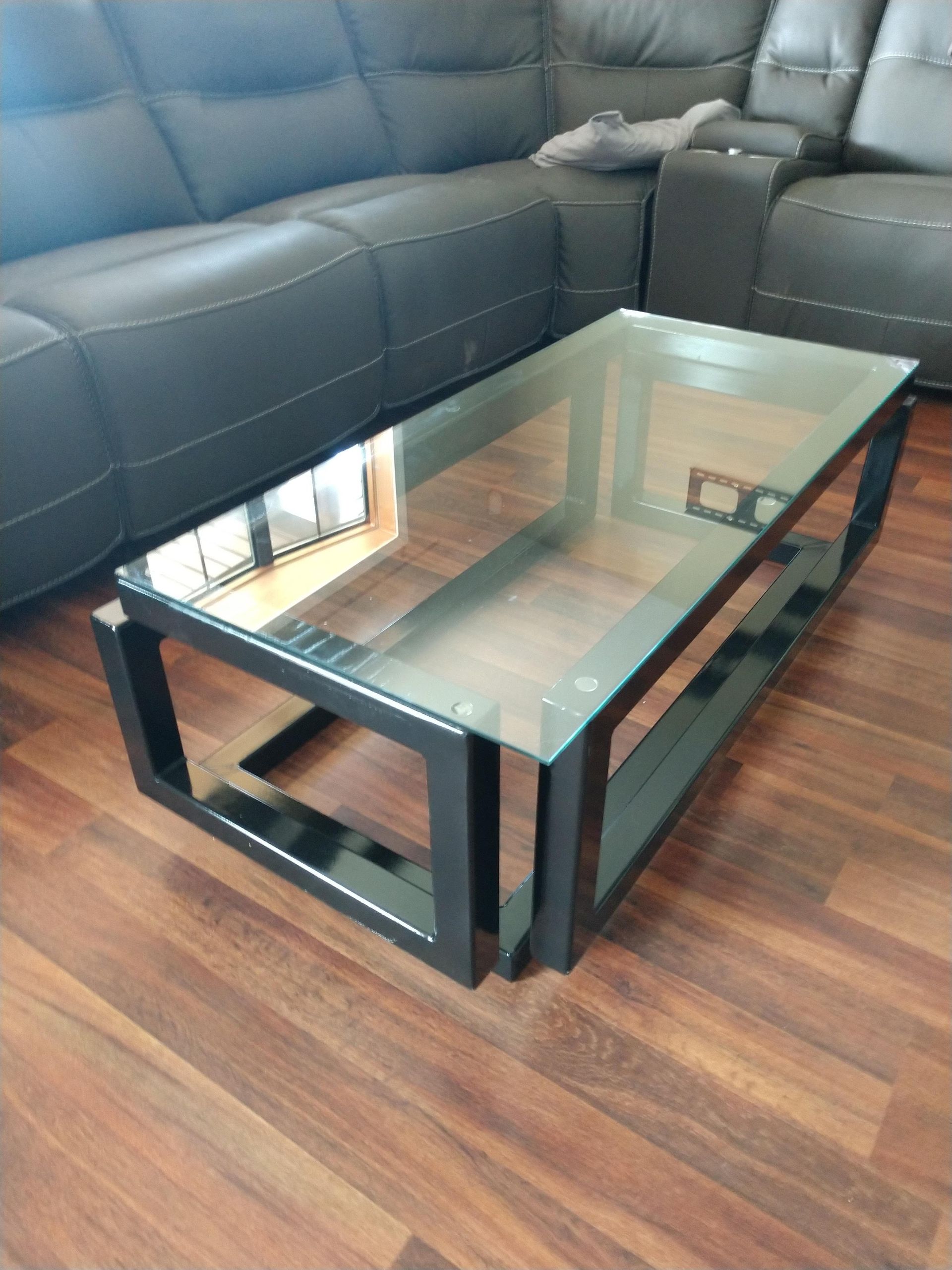 A glass coffee table is sitting in front of a couch in a living room.