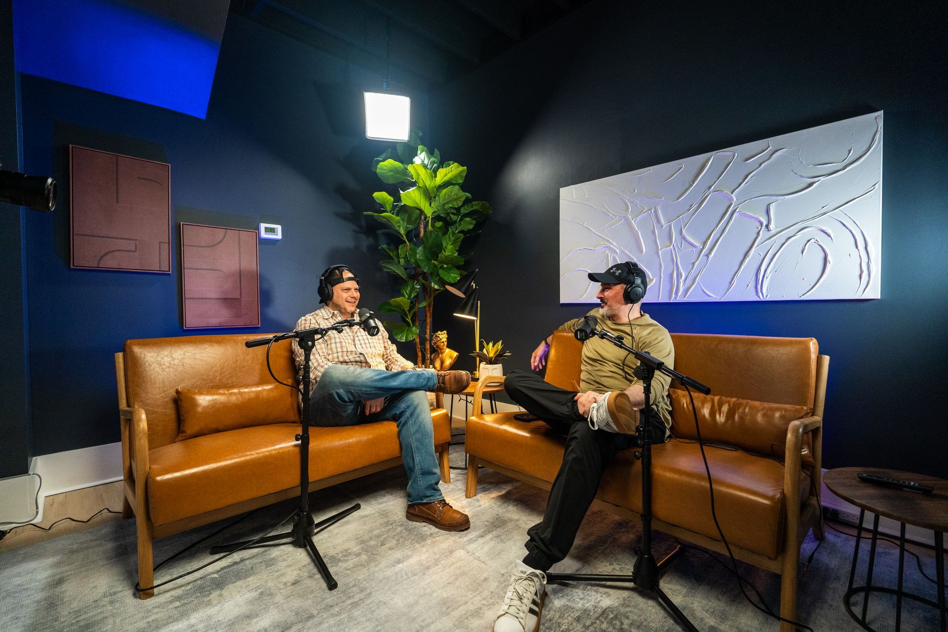 Two men are sitting on couches in front of microphones in a room recording video content for youtube
