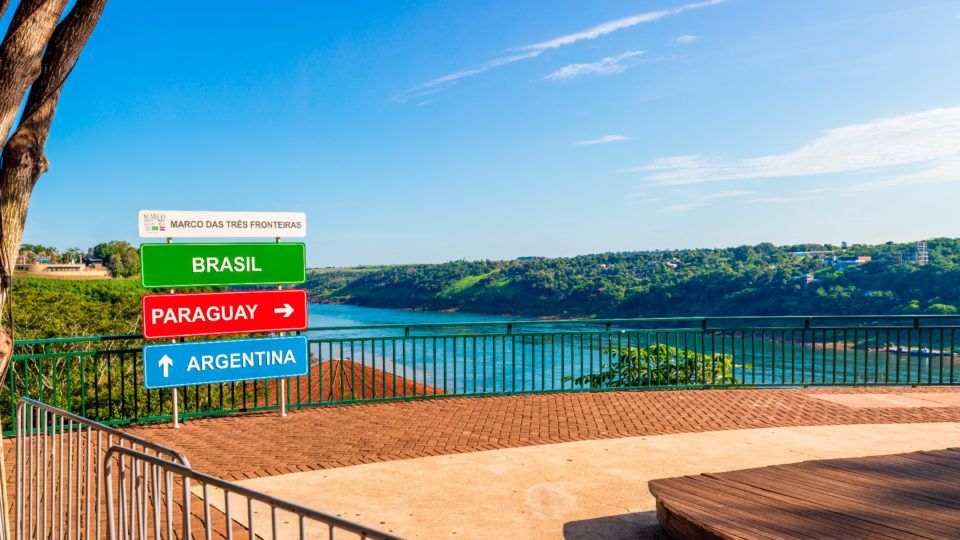 Una vista de un lago desde un balcón con carteles que apuntan a brasil, paraguay y argentina.