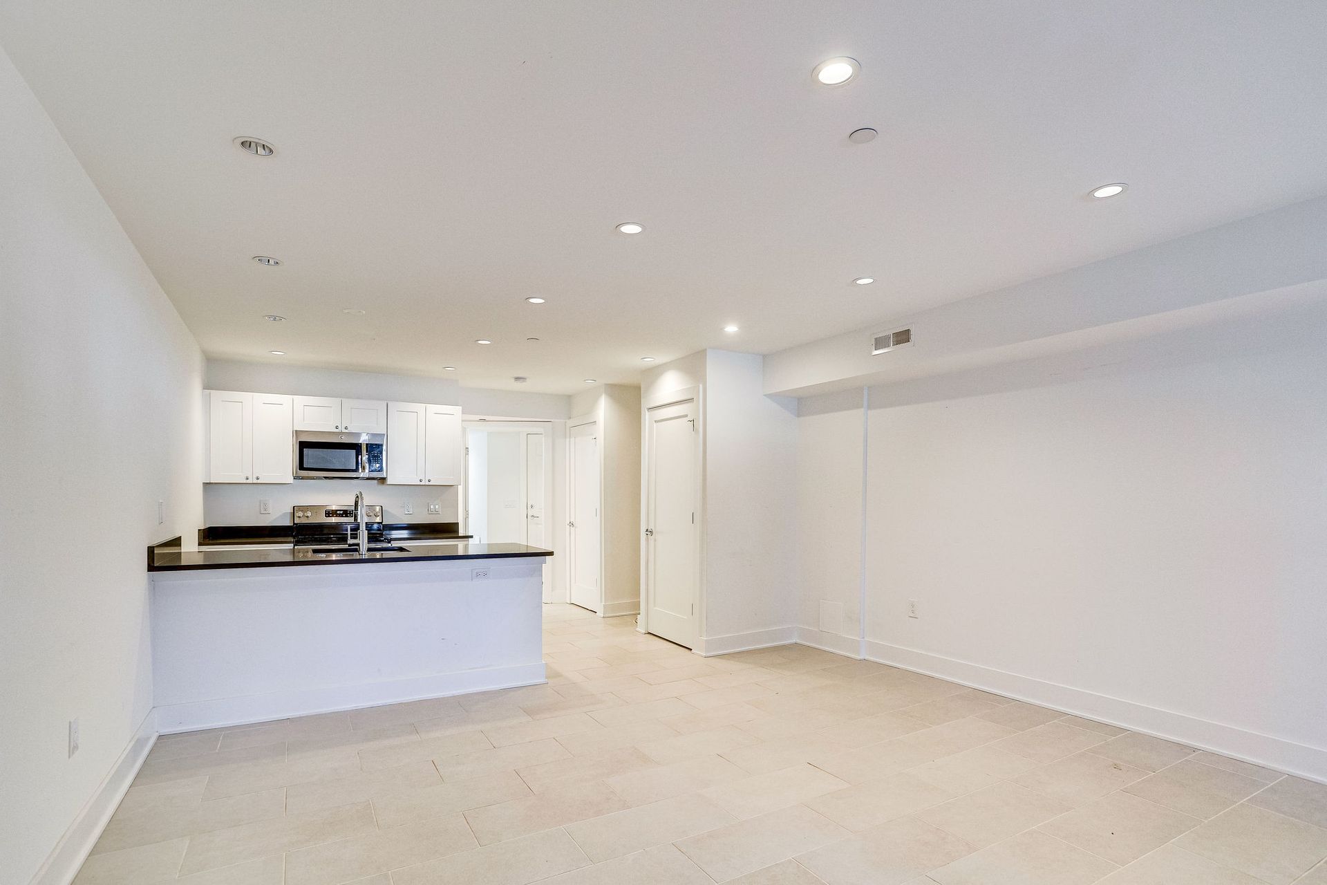 An empty living room with a kitchen in the background.