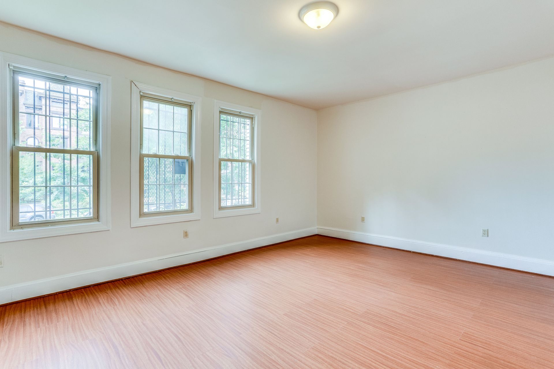 An empty room with hardwood floors and three windows.