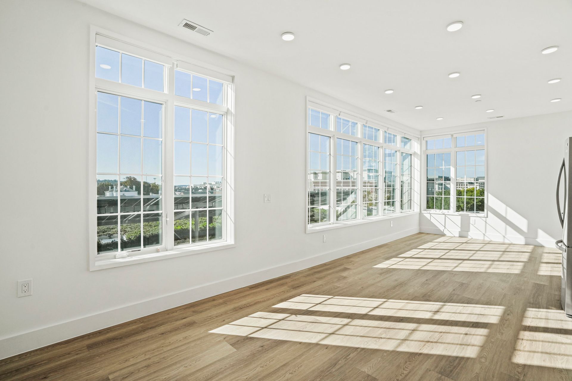 An empty living room with lots of windows and hardwood floors.