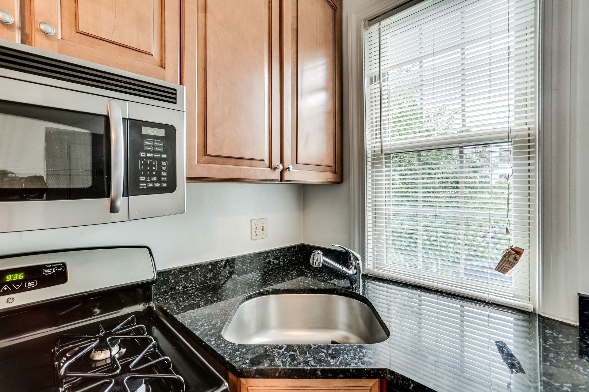 A kitchen with a sink , stove , microwave and window.