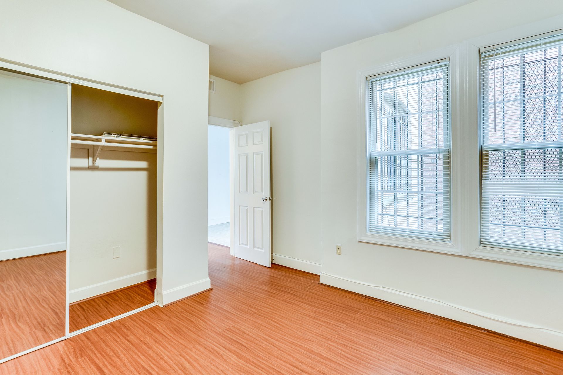 An empty bedroom with hardwood floors , a closet , and two windows.