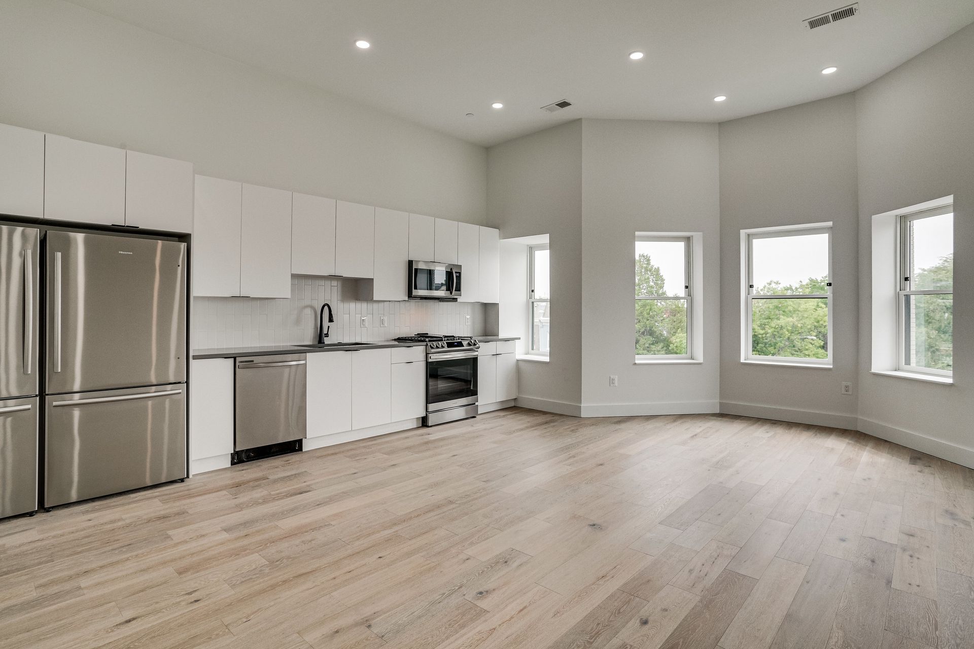 An empty kitchen with stainless steel appliances and hardwood floors.