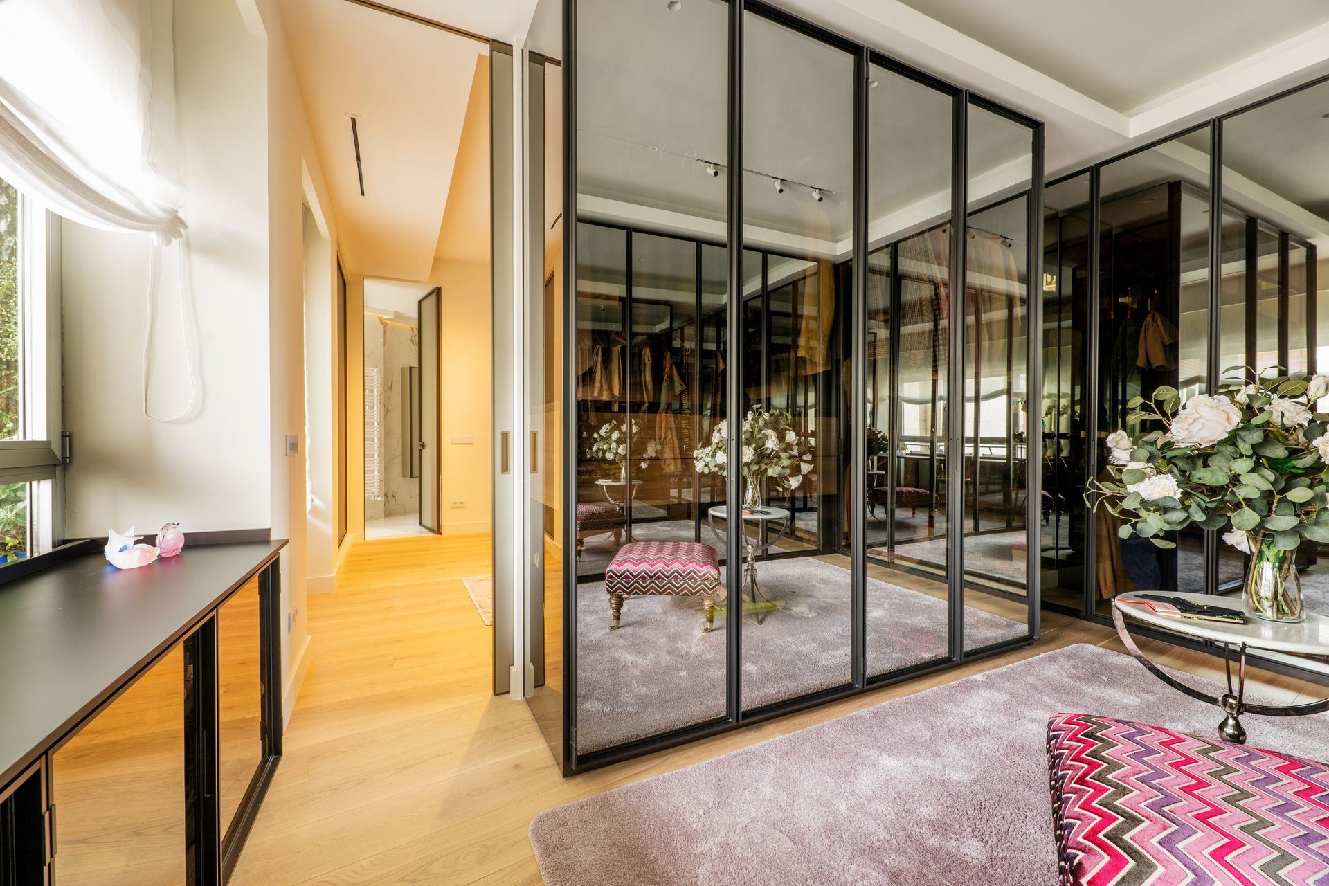Walk-in closet with mirrored doors and black frames, soft lilac carpet, and modern furniture.