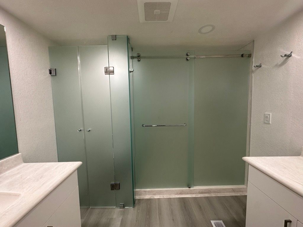 Modern bathroom with frosted glass shower enclosure, two sinks, and grey floor.