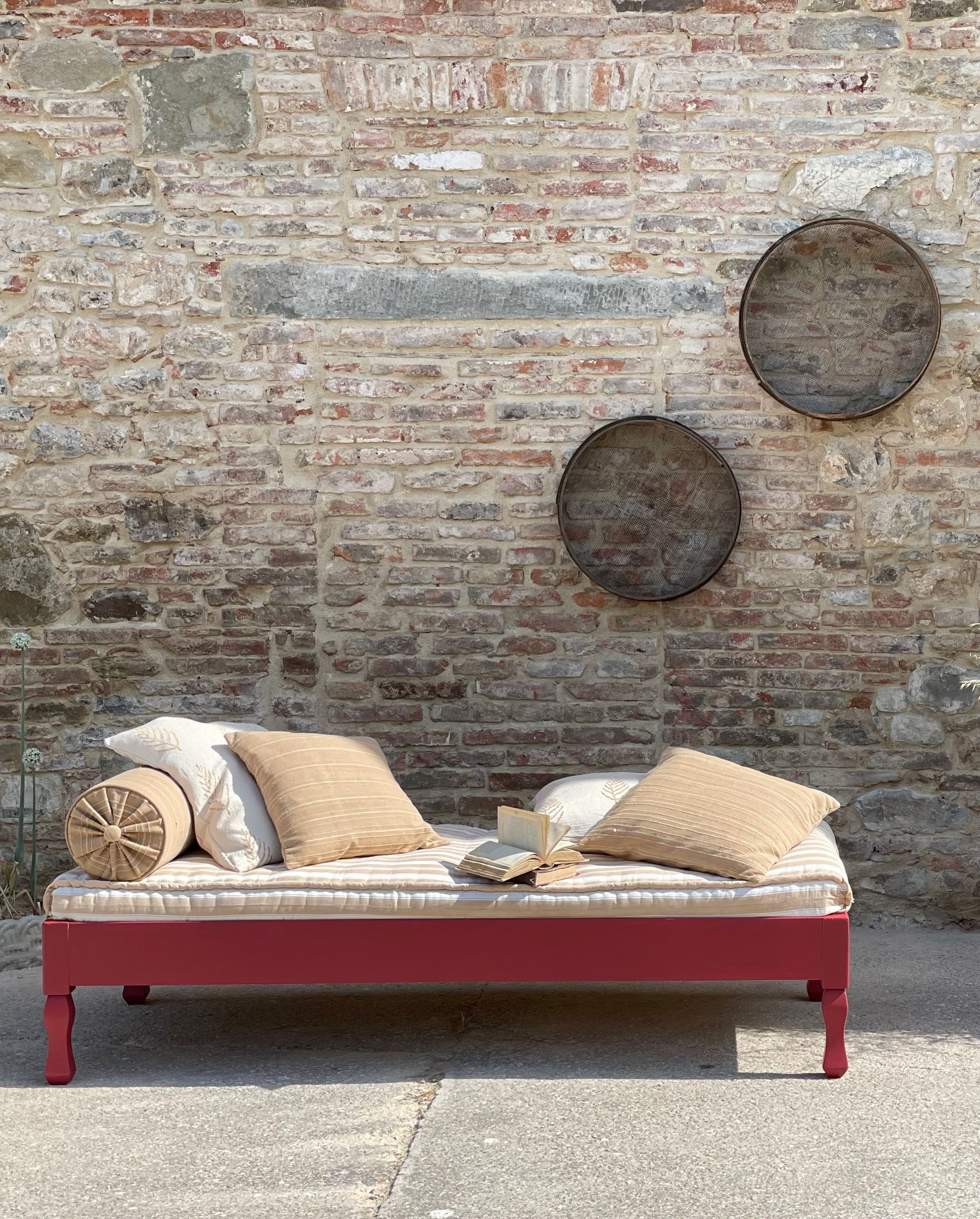 Divano letto rosso con cuscini contro un muro di mattoni, due arazzi circolari intrecciati.