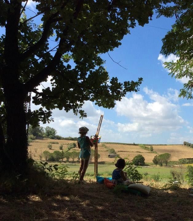 Due bambini sotto un albero dipingono un paesaggio in una giornata di sole.