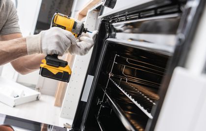Person using a yellow power drill to install an oven in a kitchen