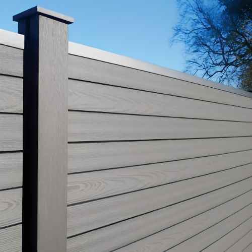 Gray privacy fence with horizontal slats and a square post against a blue sky