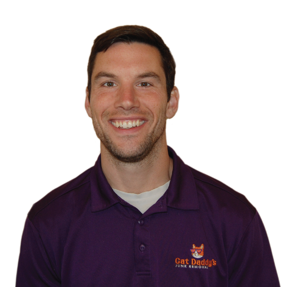Smiling man in a purple polo shirt with a logo, standing against a white background