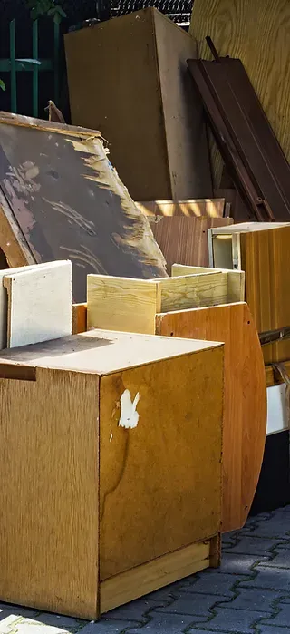 Stacked wooden cabinets and panels in an outdoor storage area next to a fence